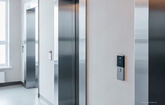 Leere Aufzugshalle mit offenen Edelstahltüren und einem an der Wand montierten Rufknopf