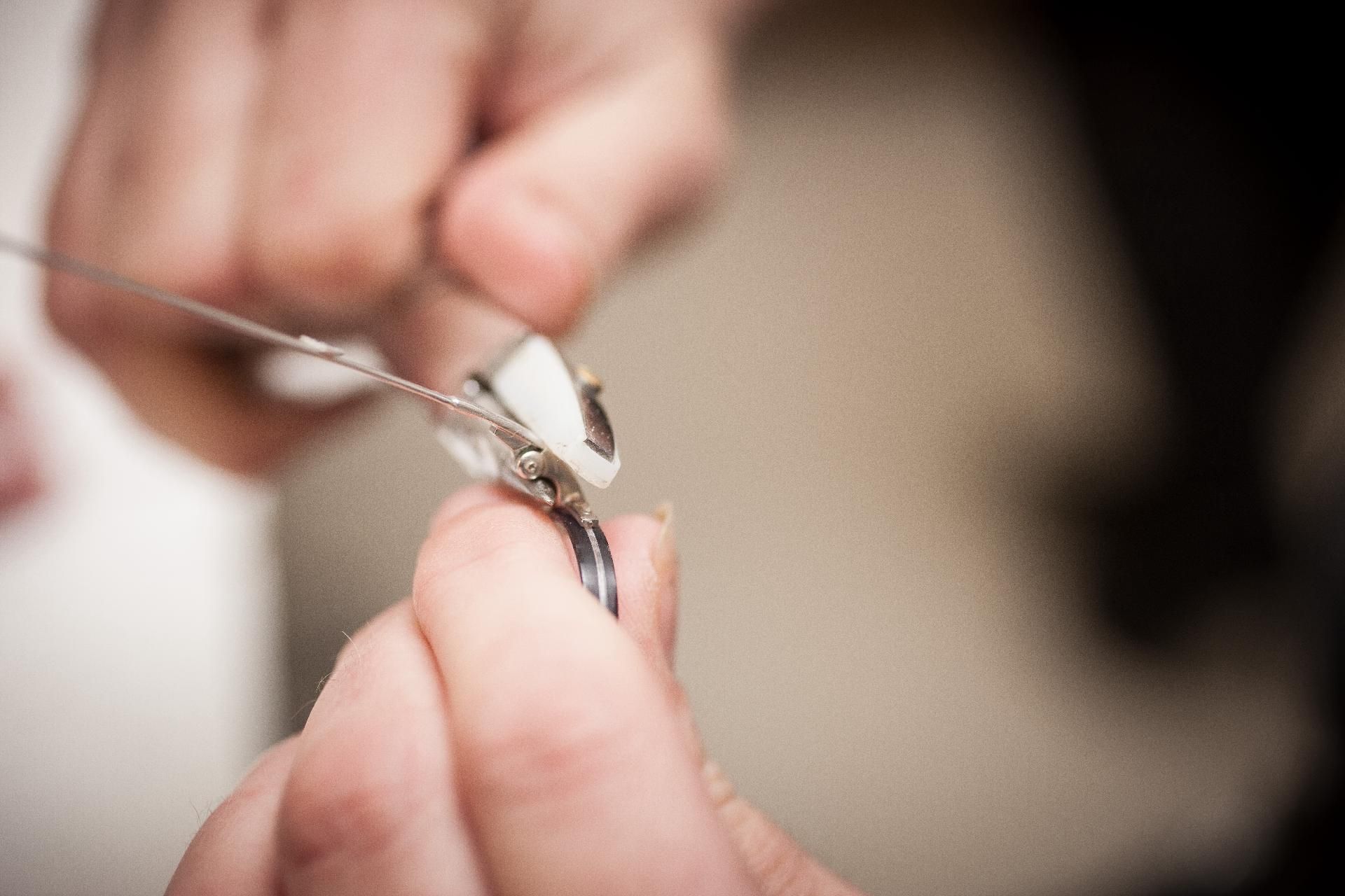 Hände halten ein kleines, weißes, mechanisches Gerät, von dem ein Draht absteht.