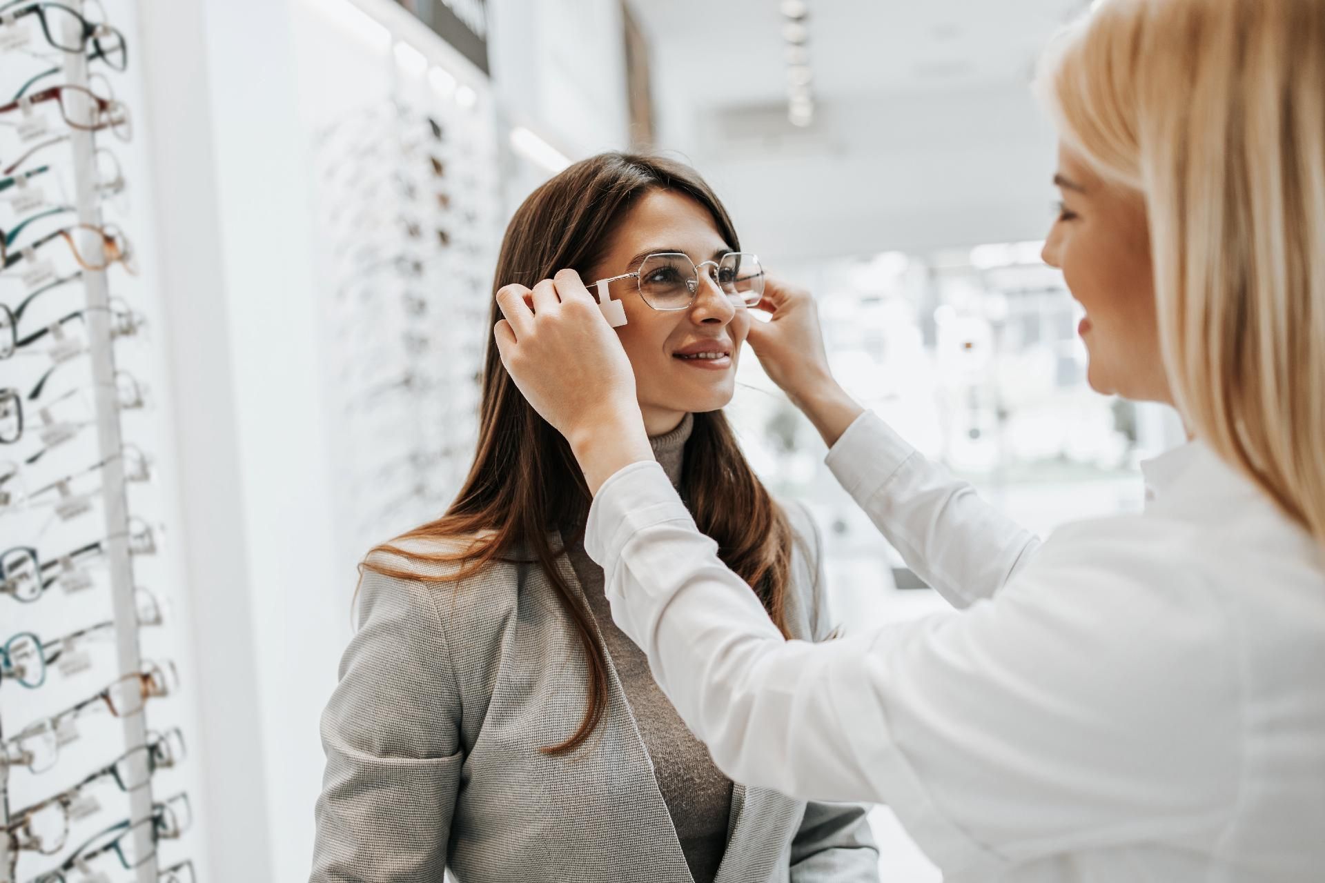 Eine Frau probiert in einem Brillengeschäft mit Hilfe eines Optikers eine Brille an.