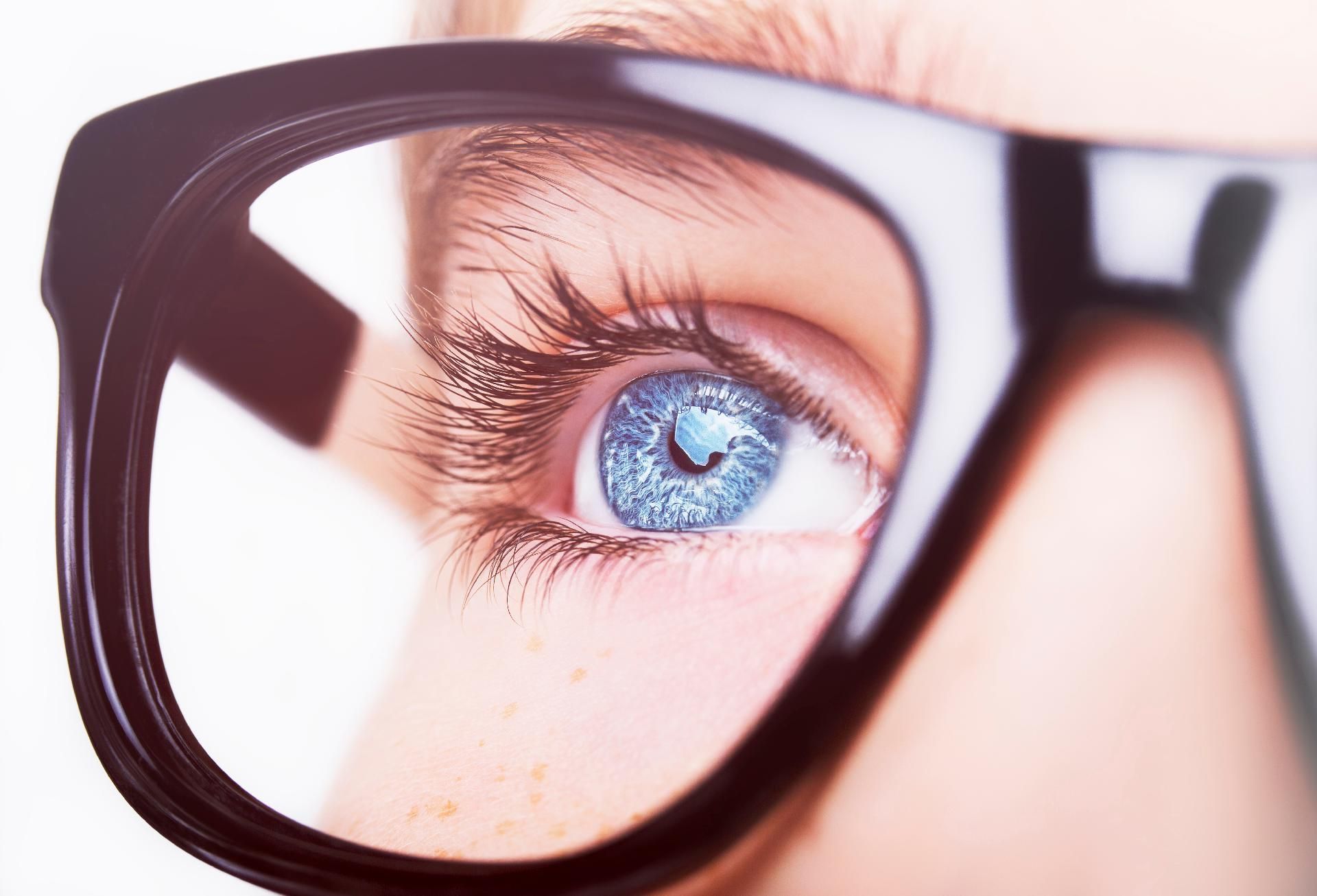 Blaue Augen mit langen Wimpern und Brille, der Blick geht durch dicke, schwarze Gläser.