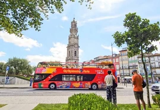 Red tour bus in a city square with Clérigos Tower in Porto in the back.