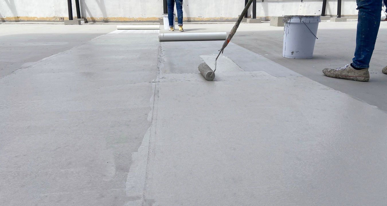 Professionnel passant un rouleau de résine étanche grise sur un toit recouvert d'une couche d'isolant