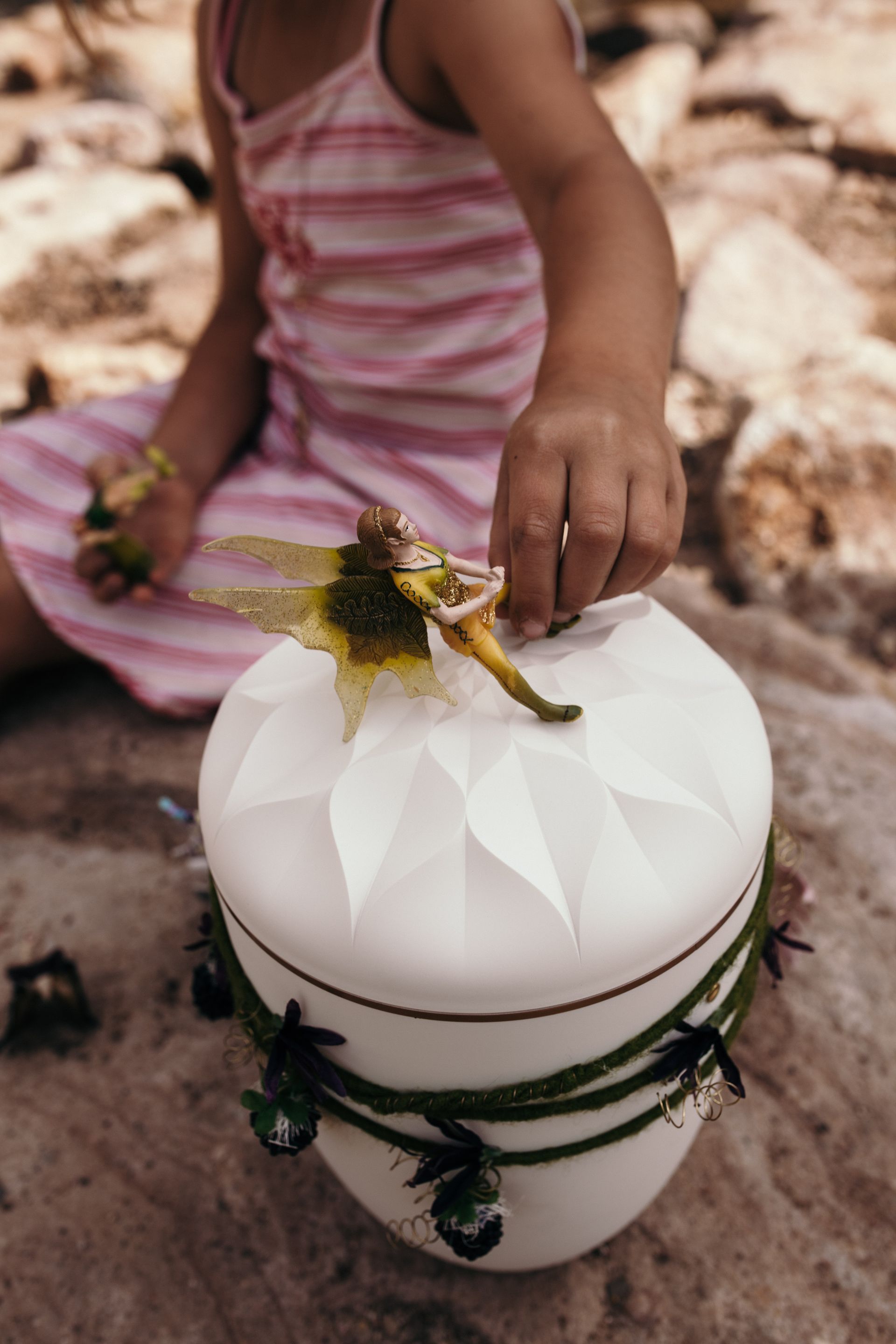 Kind stellt Feenfigur auf eine dekorierte weiße Urne.