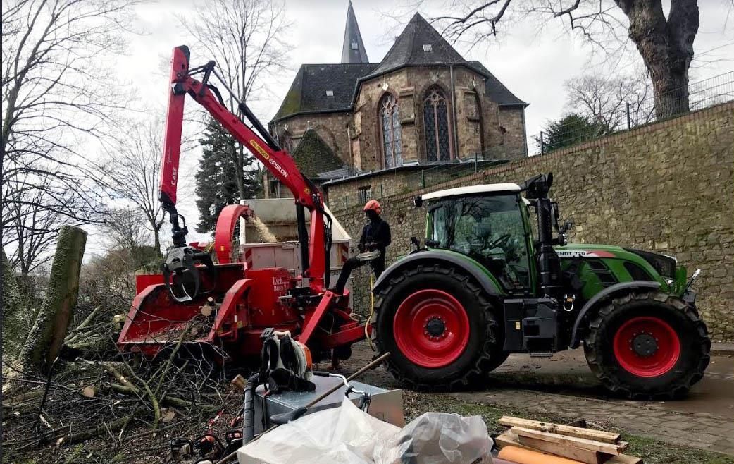 Ein Mann steht neben einem Traktor, an dem ein Kran befestigt ist.