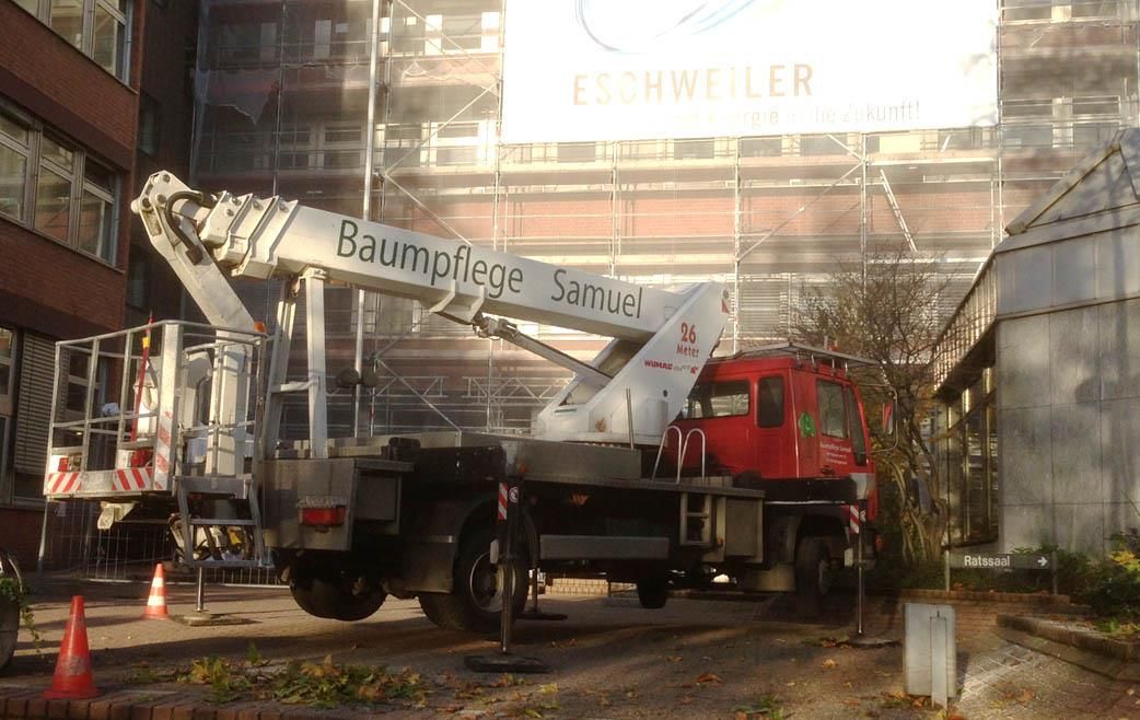 Ein roter Lastwagen mit einem Kran auf der Rückseite steht vor einem Gebäude, auf dem ein Gerüst steht