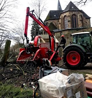 Ein Traktor fällt einen Baum vor einer Kirche.