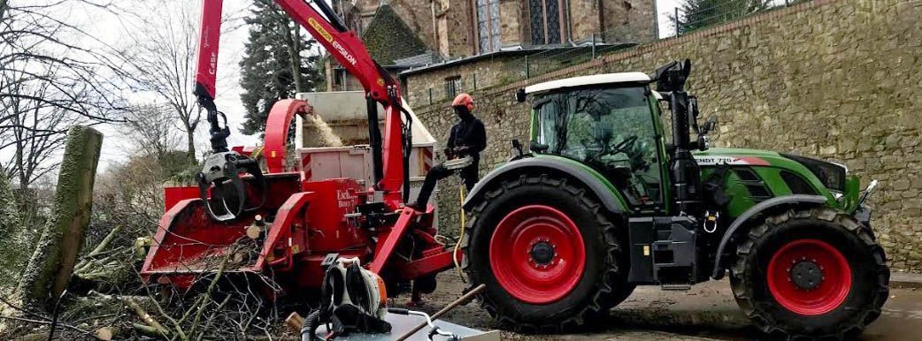 Ein Mann steht neben einem Traktor, an dem ein Kran befestigt ist.