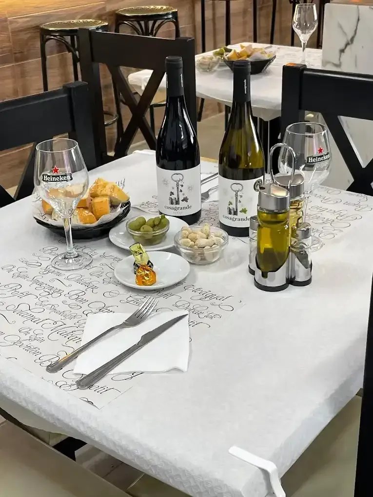 Mesa de restaurante preparada con botellas de vino, aperitivos y cubiertos.