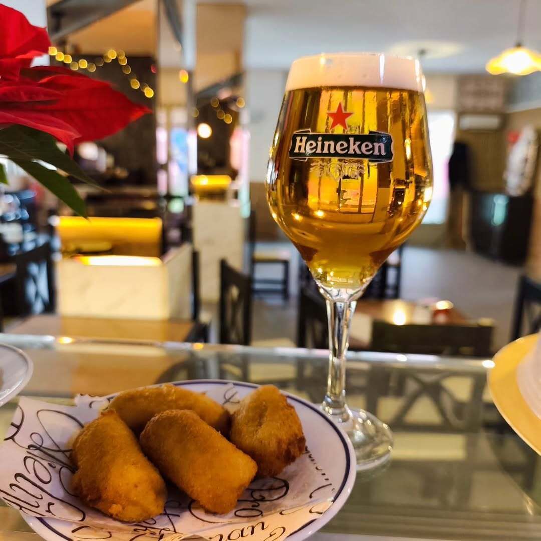 Cerveza Heineken en vaso con croquetas en plato en un ambiente de bar.