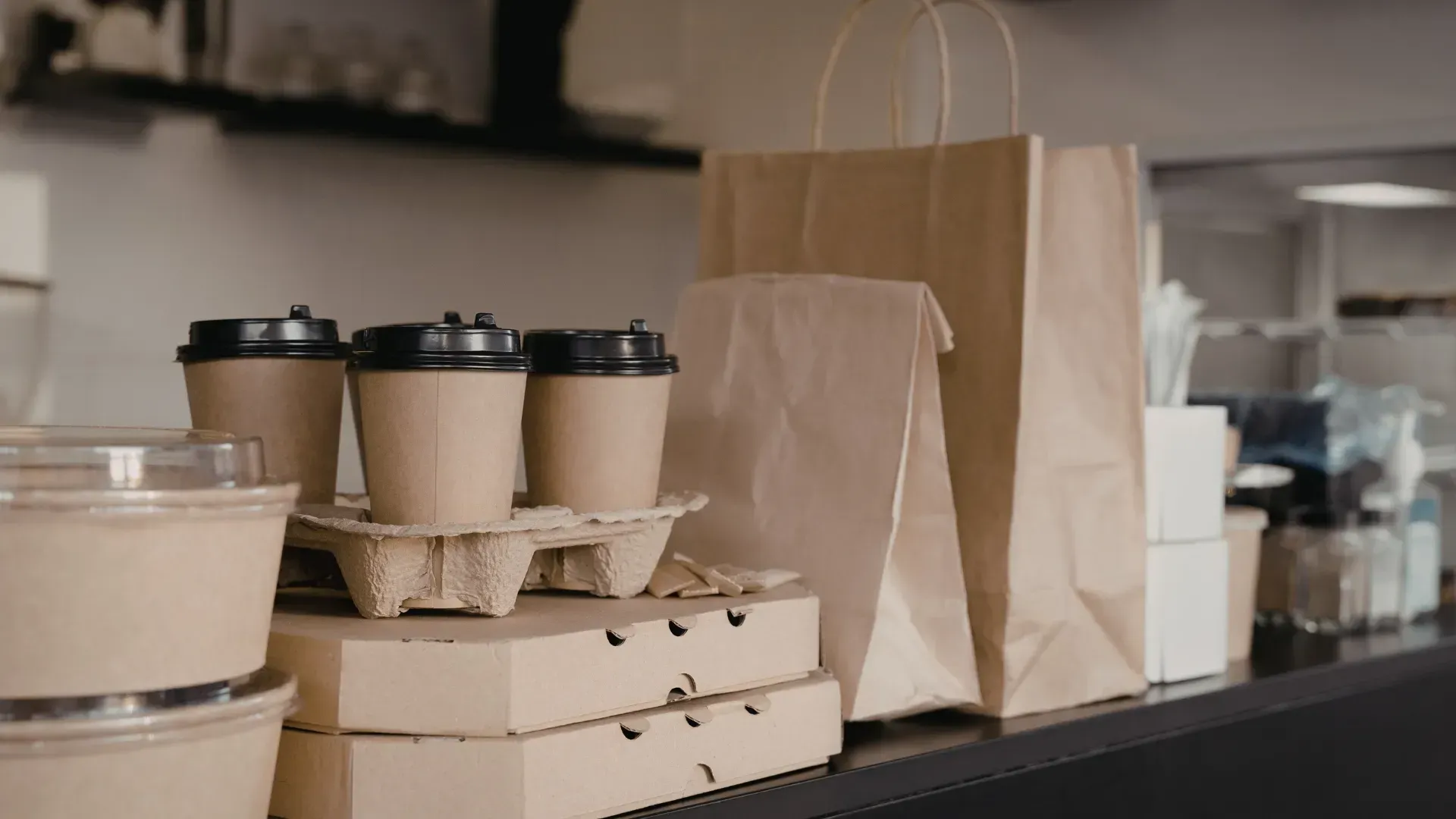 Contenedores marrones para llevar, vasos de café, bolsas de papel y cajas sobre un mostrador.