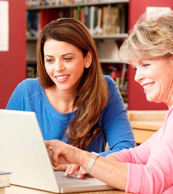 Dos mujeres miran juntas una computadora portátil y sonríen.
