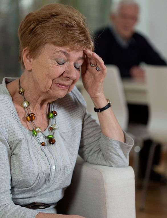 Una anciana está sentada en un sofá con la mano en la frente.
