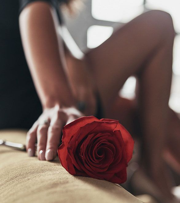 Una mujer está sentada en una cama sosteniendo una rosa roja.