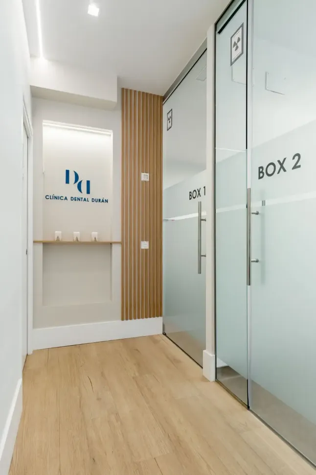 Pasillo de una clínica médica con dos salas de examen con puertas de vidrio, piso de madera y el logotipo de la clínica.