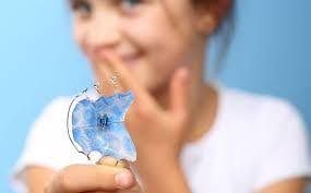 Niña sosteniendo un retenedor dental azul, sonriendo.