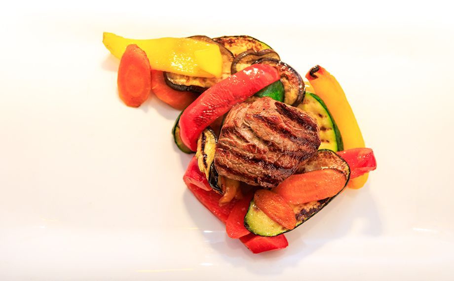 Gegrilltes Fleisch und Gemüse auf einem weißen Teller: rote und gelbe Paprika, Zucchini und Karotten.