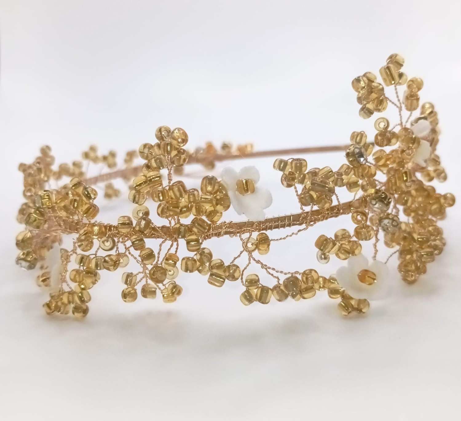 Diadema floral dorada con detalles de perlas blancas sobre fondo blanco.