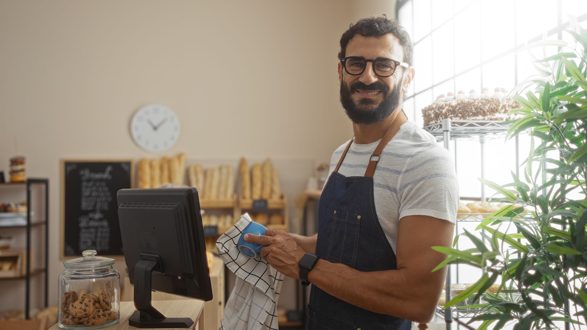 Un homme en tablier nettoie le comptoir d'une boulangerie, en souriant.