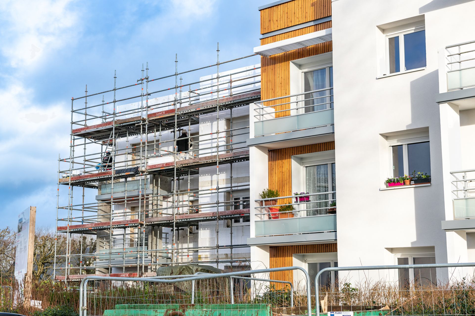 Bâtiment avec échafaudages pour rénovation ; murs blancs, éléments en bois, balcons.