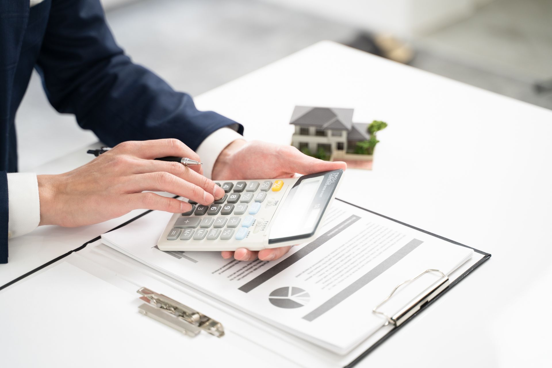 Une personne en costume utilise une calculatrice sur des documents représentant une maquette de maison.