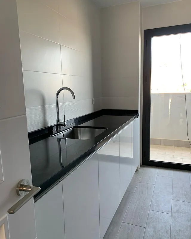 Una cocina con fregadero, grifo y puerta corrediza de cristal.