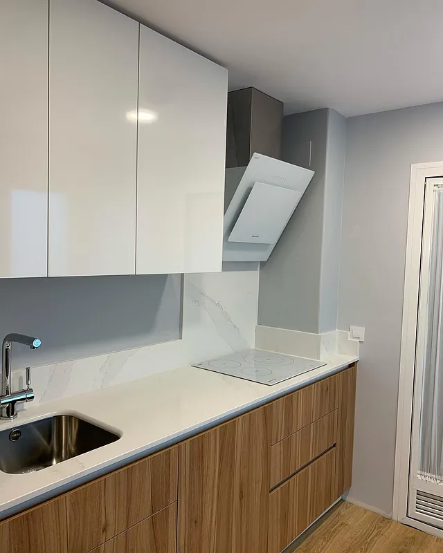 Una cocina con gabinetes blancos, gabinetes de madera, un fregadero y un horno de estufa.