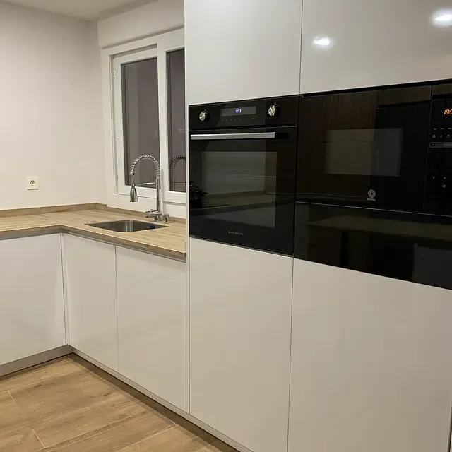 Una cocina con gabinetes blancos, electrodomésticos negros, un fregadero y una ventana.