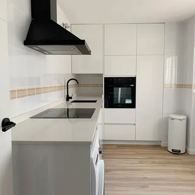 Una cocina con gabinetes blancos, un horno, un fregadero y un bote de basura.