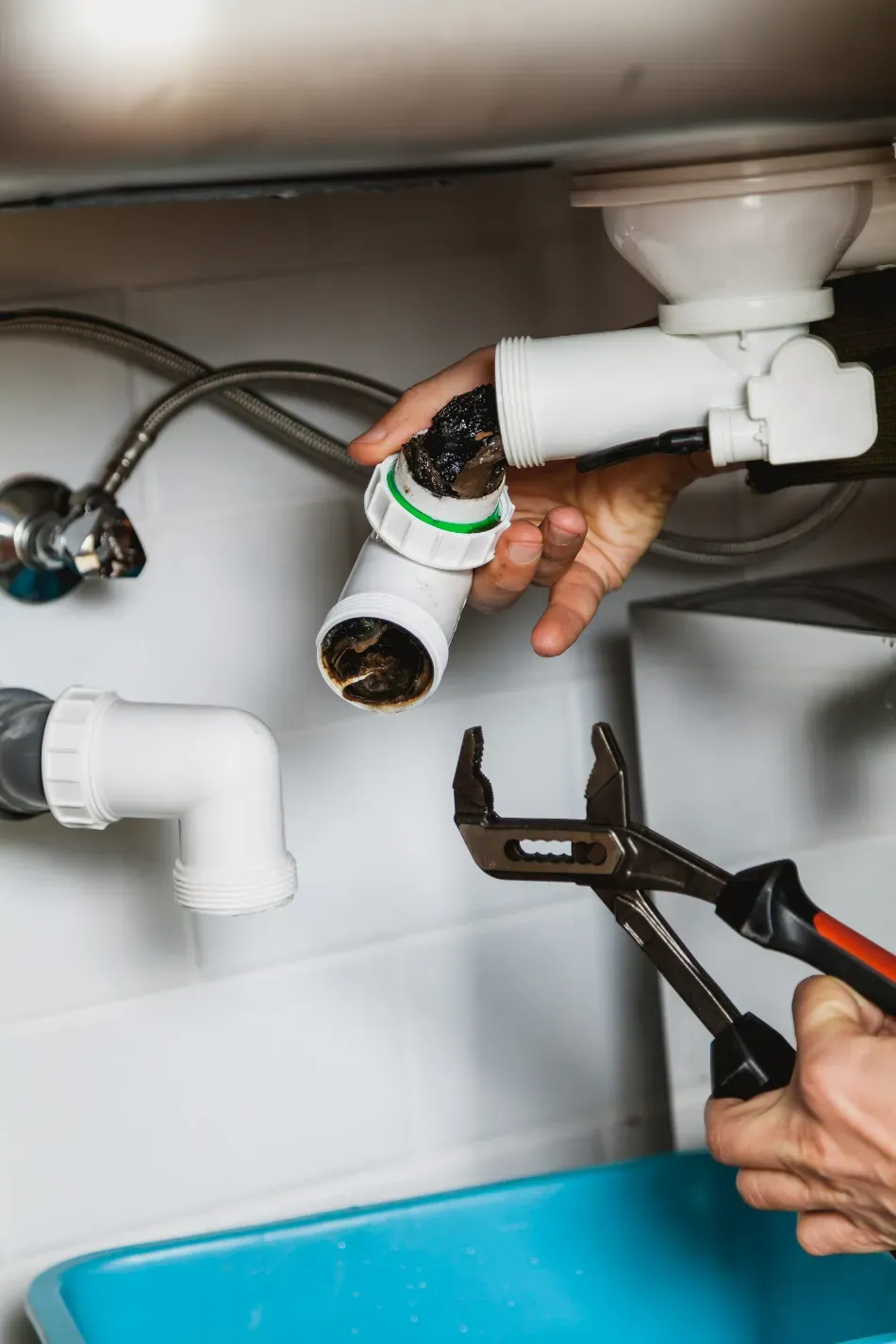 Manos reparando un tubo de desagüe blanco debajo de un lavabo de baño con una llave inglesa.