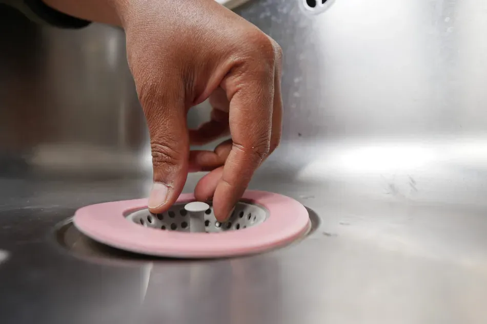 Colocando a mano un colador rosa en el desagüe de un fregadero de acero inoxidable.
