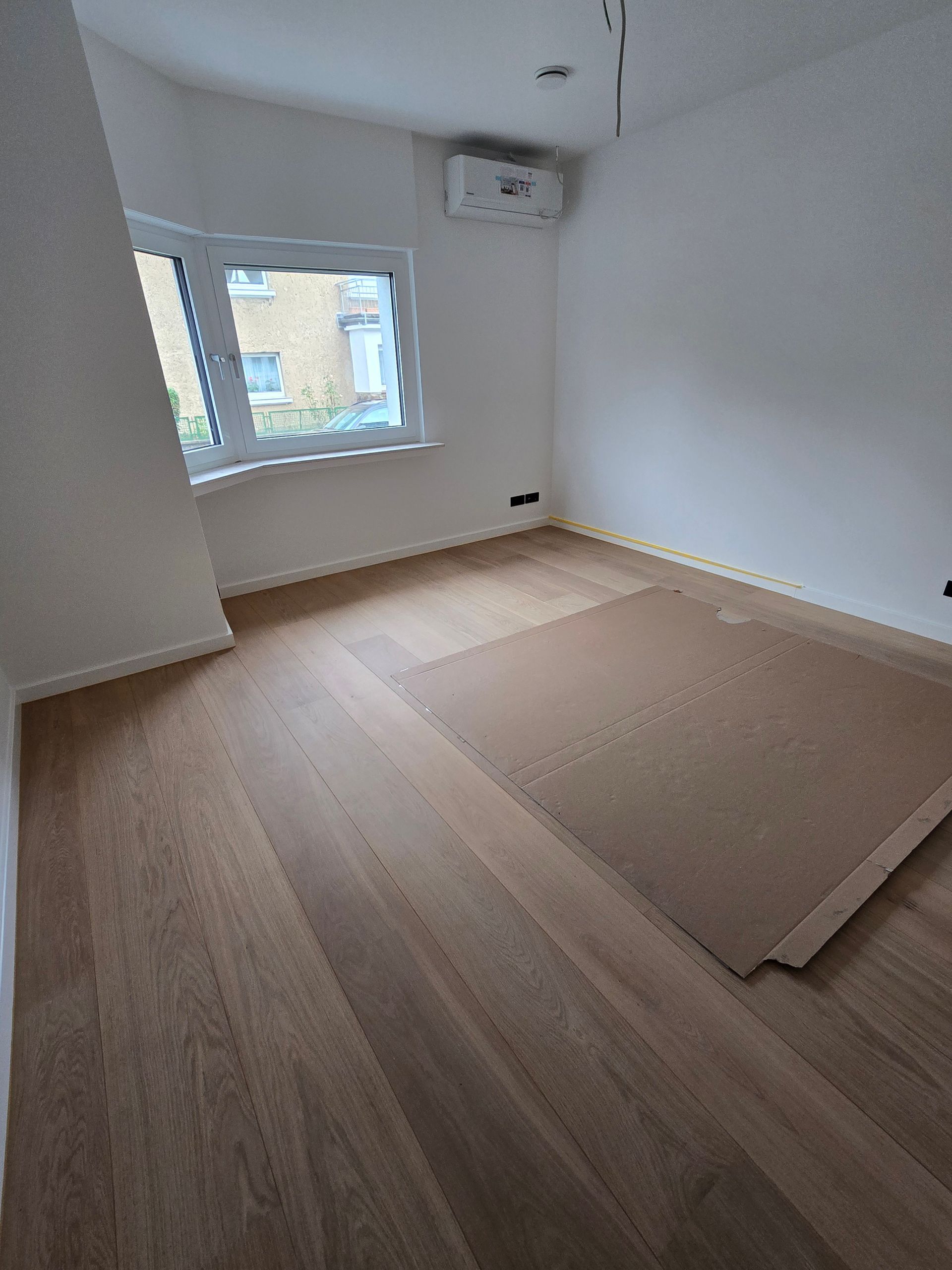 Leeres Zimmer mit Holzboden, Fenster und Klimaanlage.