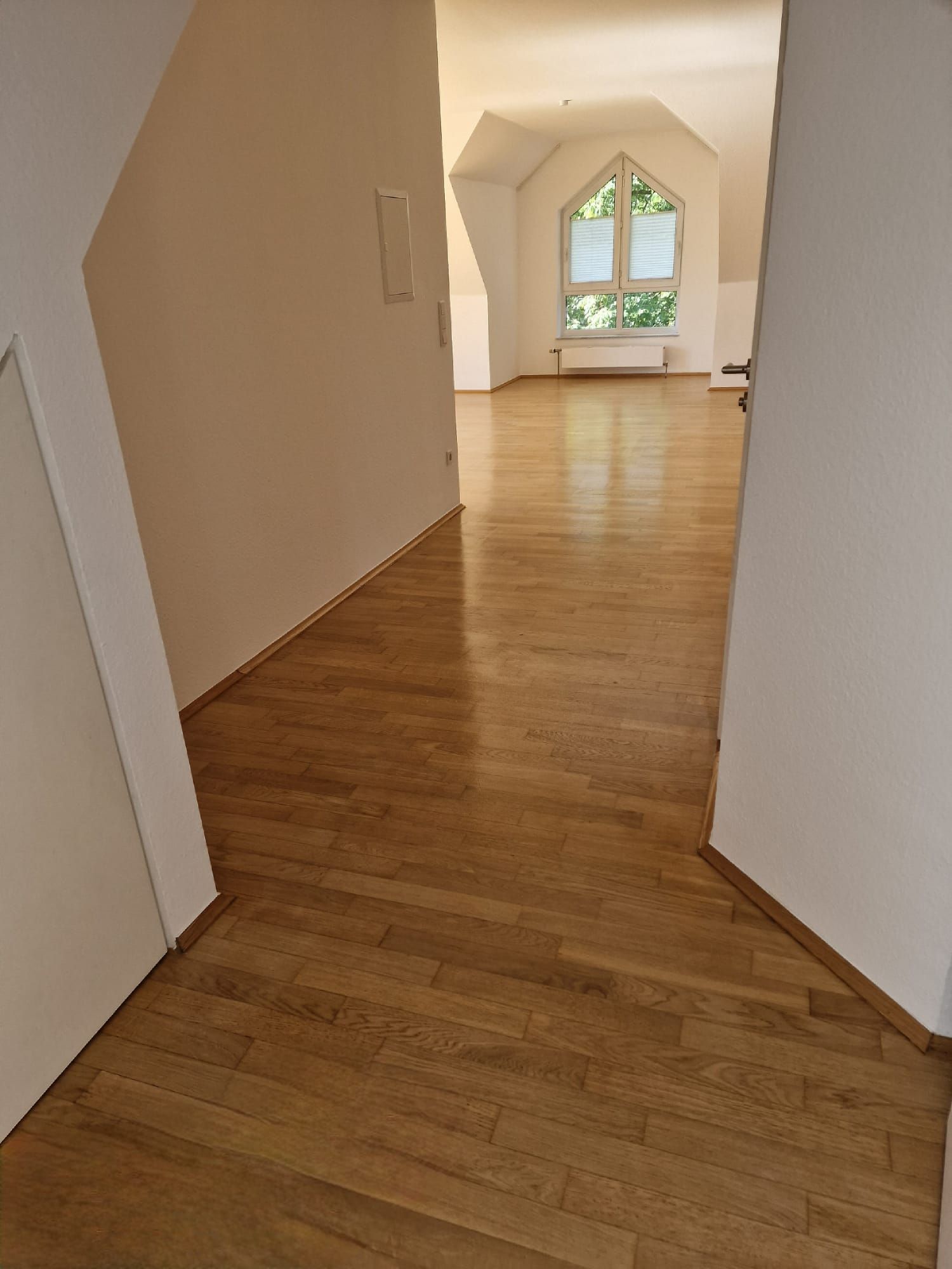 Ein hölzerner Flur führt zu einem hellen Zimmer mit großem Fenster.