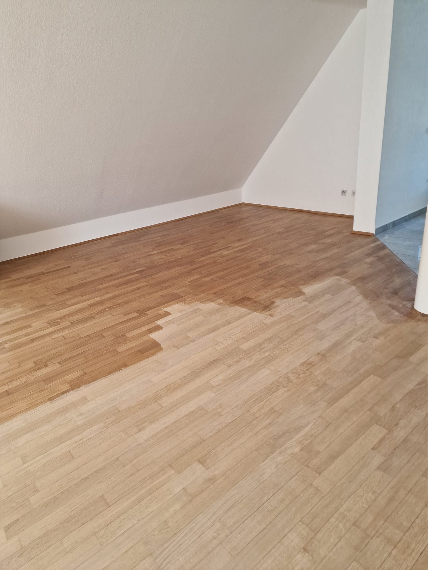 Teilweise gebeizter Holzboden in einem Zimmer mit weißen Wänden.
