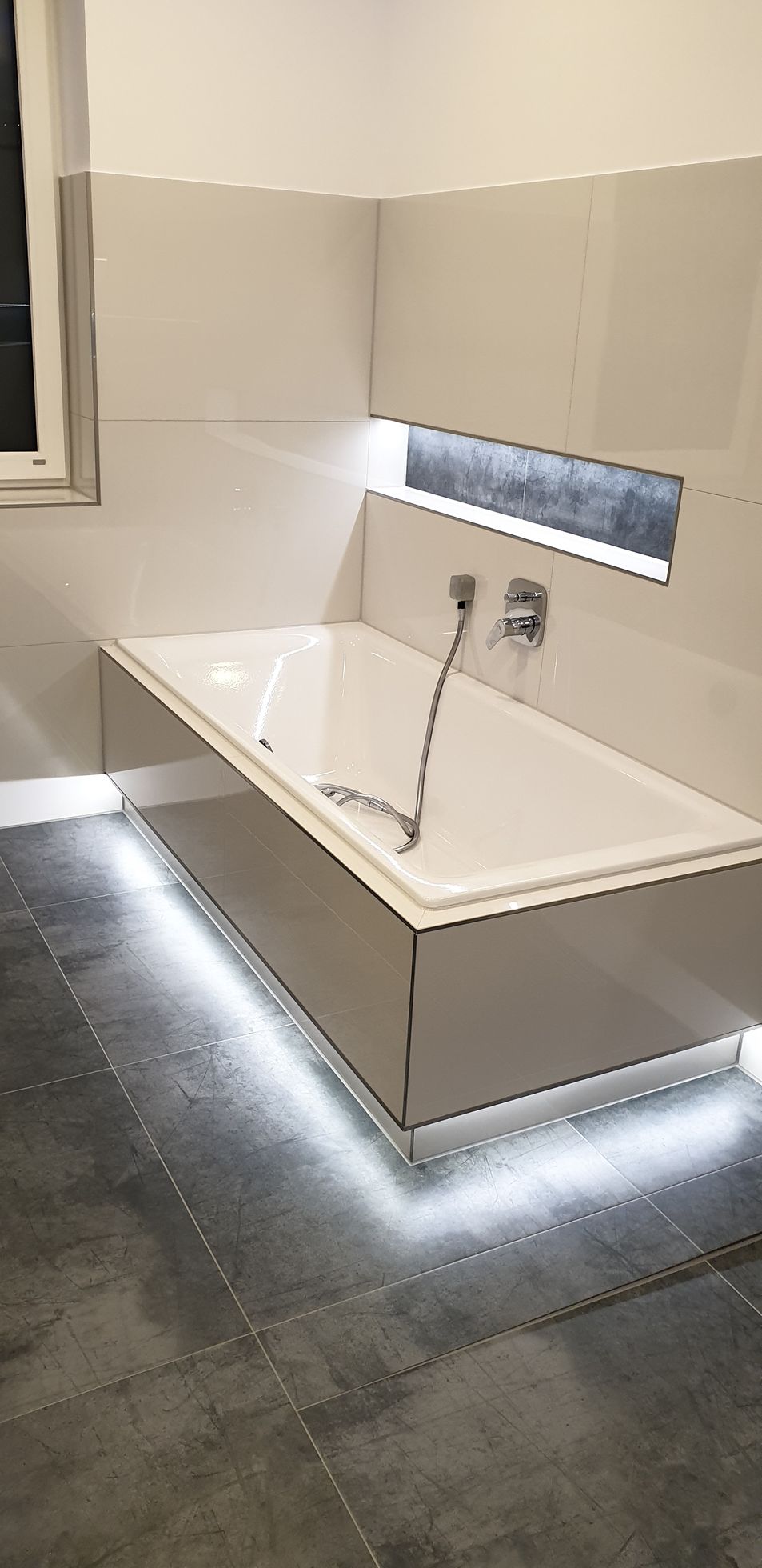 Ein modernes Badezimmer mit weißer Badewanne, die von LED-Leuchten von unten beleuchtet wird.