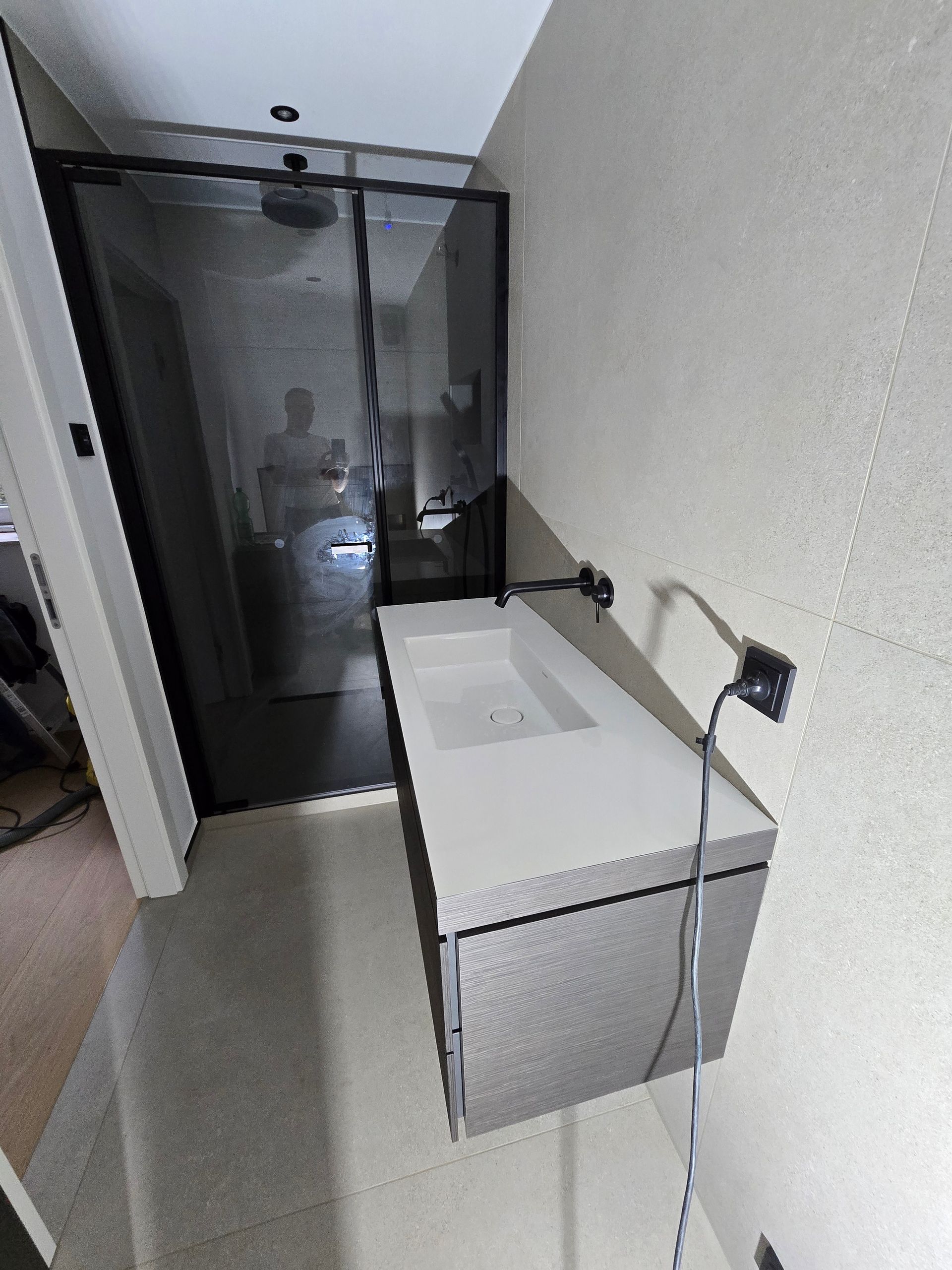 Modernes Badezimmer mit schwebendem Waschtisch, Duschkabine aus Glas und dunklen Armaturen.