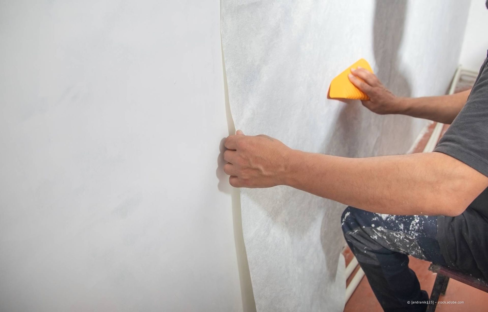 Eine Person glättet mit einem gelben Glättwerkzeug Tapeten auf einer weißen Wand.