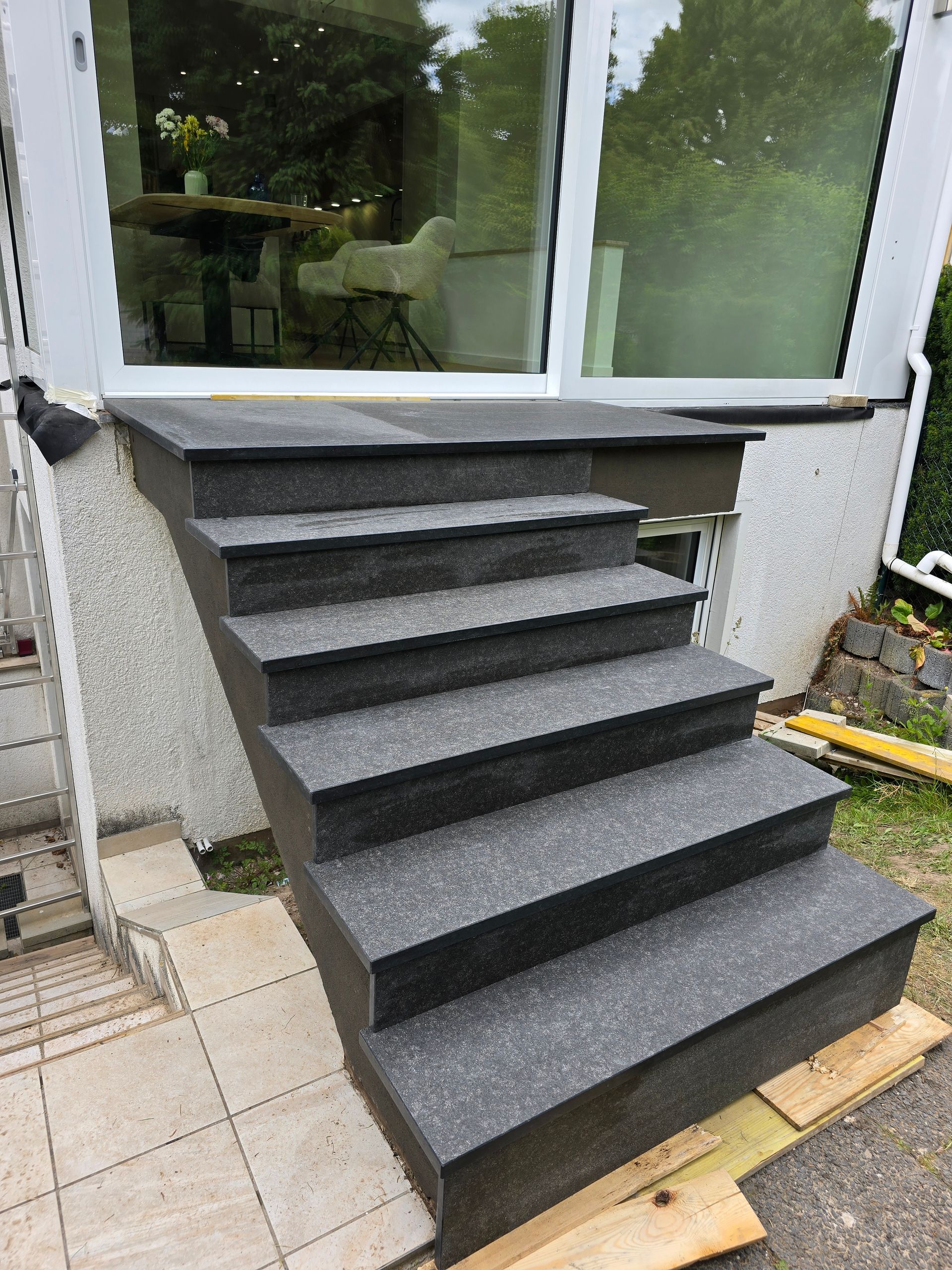 Graue Steinstufen führen hinauf zu einem Haus mit großen Fenstern.