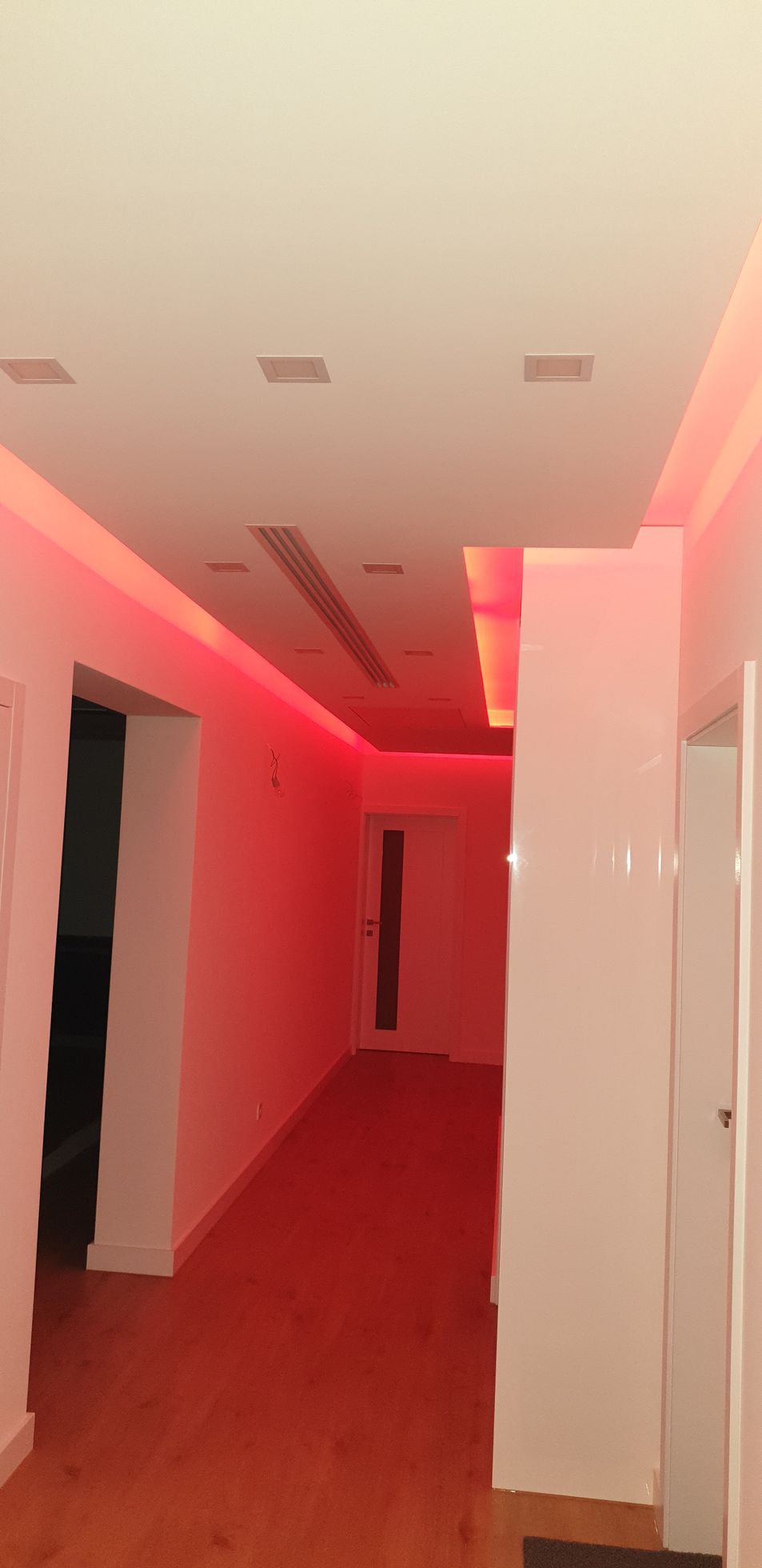 Ein Flur mit roter Beleuchtung an Decke und Wänden. Holzboden und weiße Säulen.