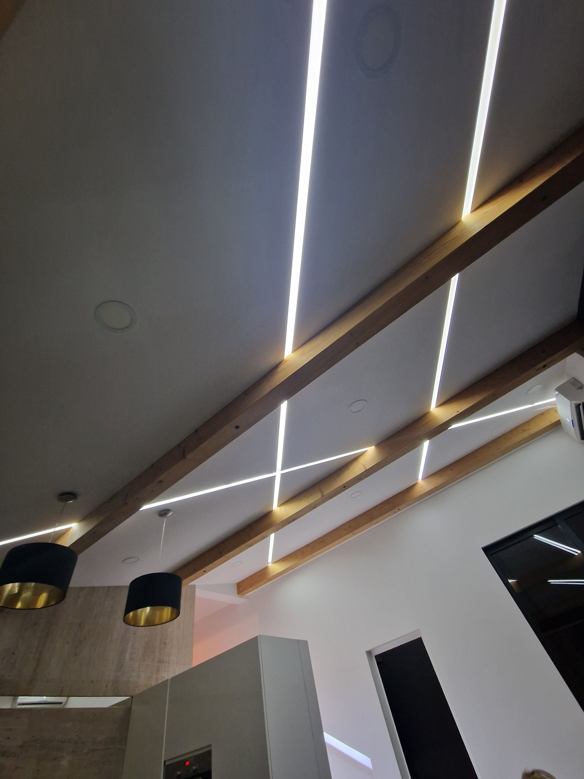 Schräge Decke mit Holzbalken und linearen LED-Leuchten.