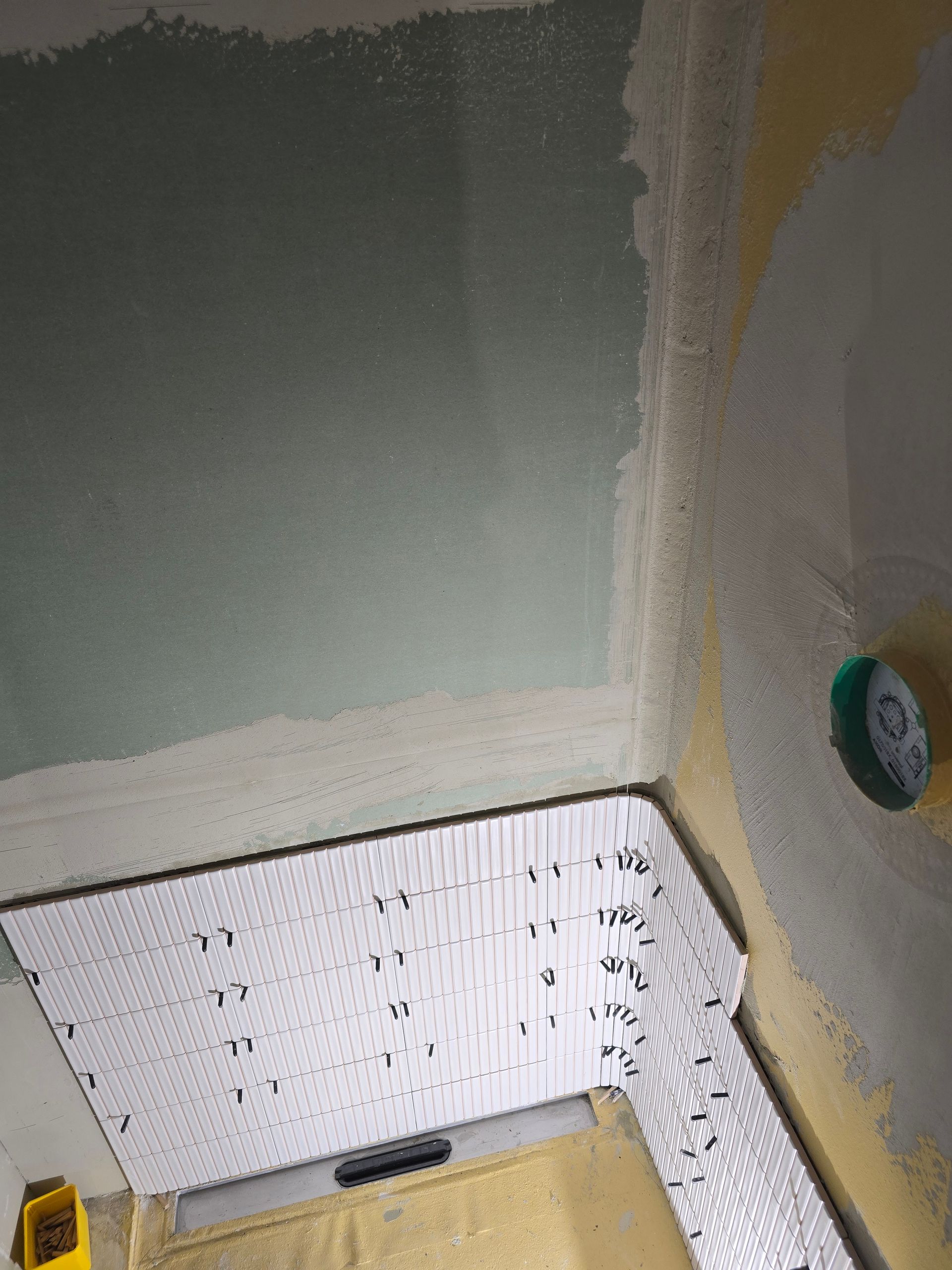 Ecke eines Raumes mit Baustelle, einem Nivelliergerät und Messmarkierungen auf einer weißen Tafel.