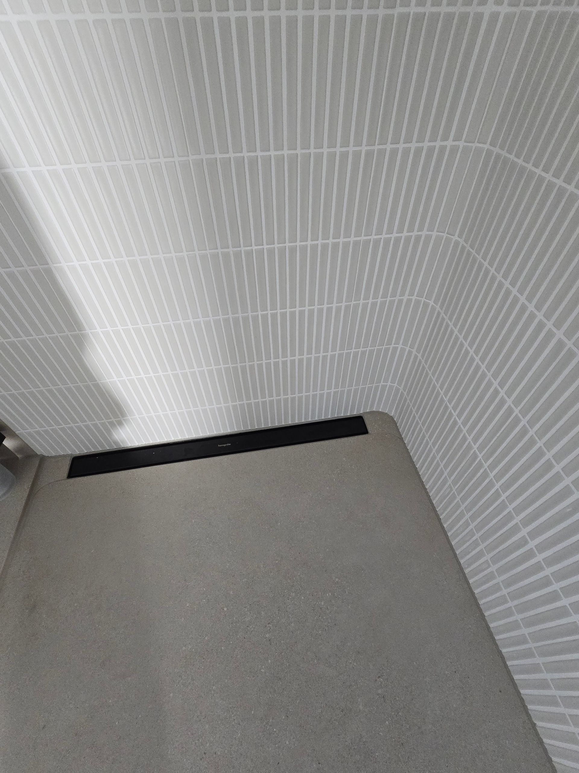 Eine graue Fliesenwand geht in eine graue Bank mit einem schwarzen Streifen am Rand über.