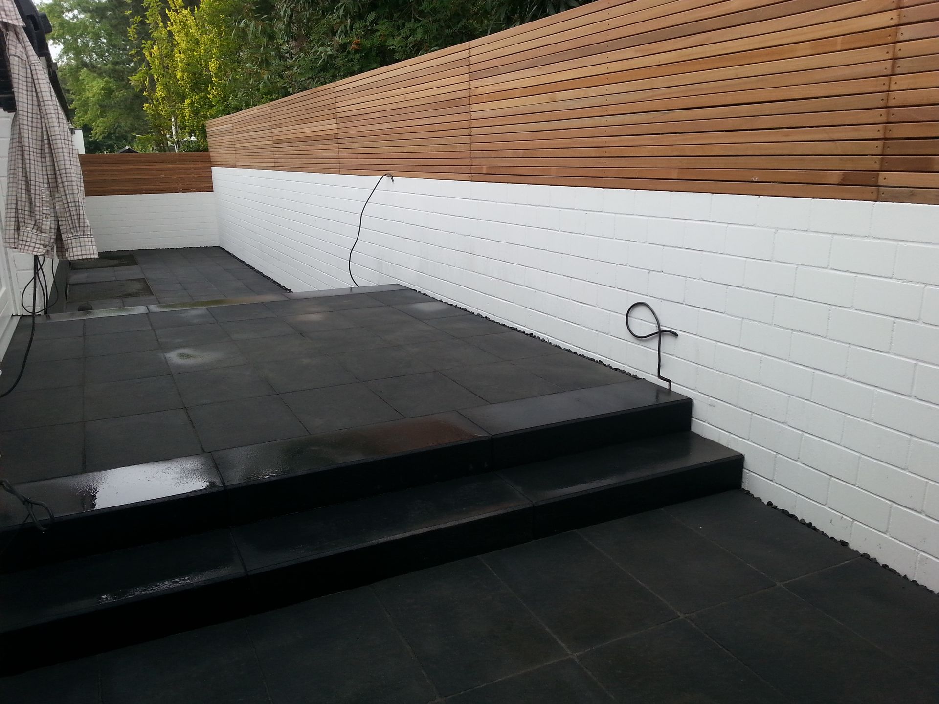 Schwarze, geflieste Terrasse mit Stufen, weiße, strukturierte Wände und Holzzaun.