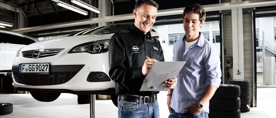 Zwei Männer schauen auf ein Klemmbrett vor einem weißen Auto.