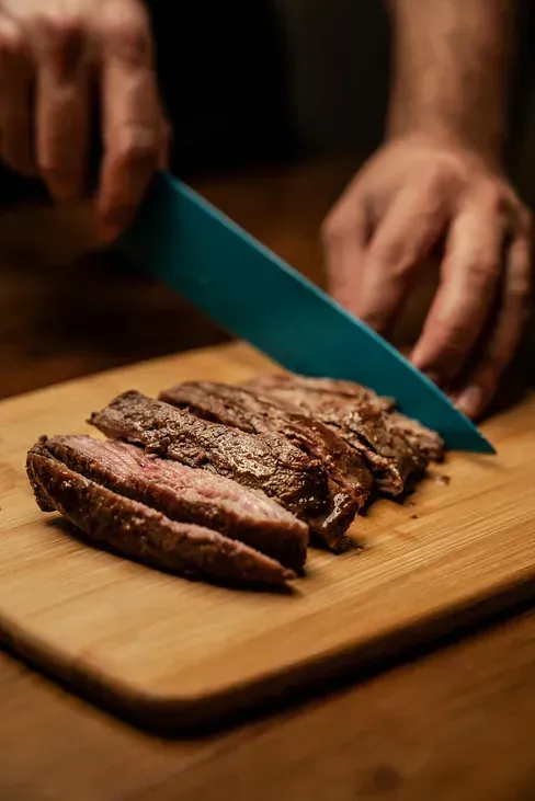 Una persona está cortando un trozo de carne en una tabla de cortar.