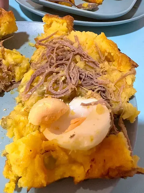 Un primer plano de un trozo de comida con carne y huevos en un plato.