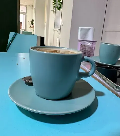 Una taza de café reposa sobre un platillo sobre una mesa azul.