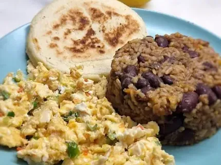 Un plato azul cubierto con huevos revueltos, arroz y frijoles.