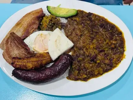 Un plato de comida con frijoles, huevos, tocino, salchicha y aguacate en una mesa.