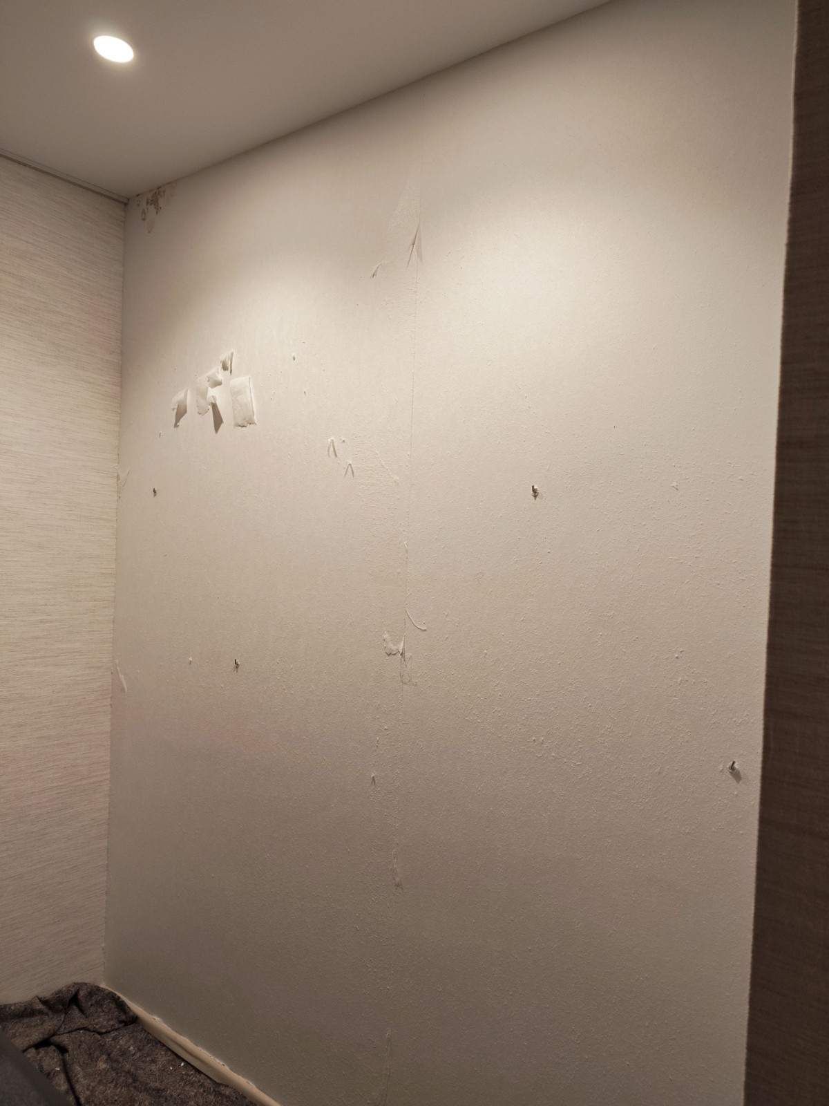 Pared blanca desnuda con pequeños puntos desconchados en una habitación con poca luz.