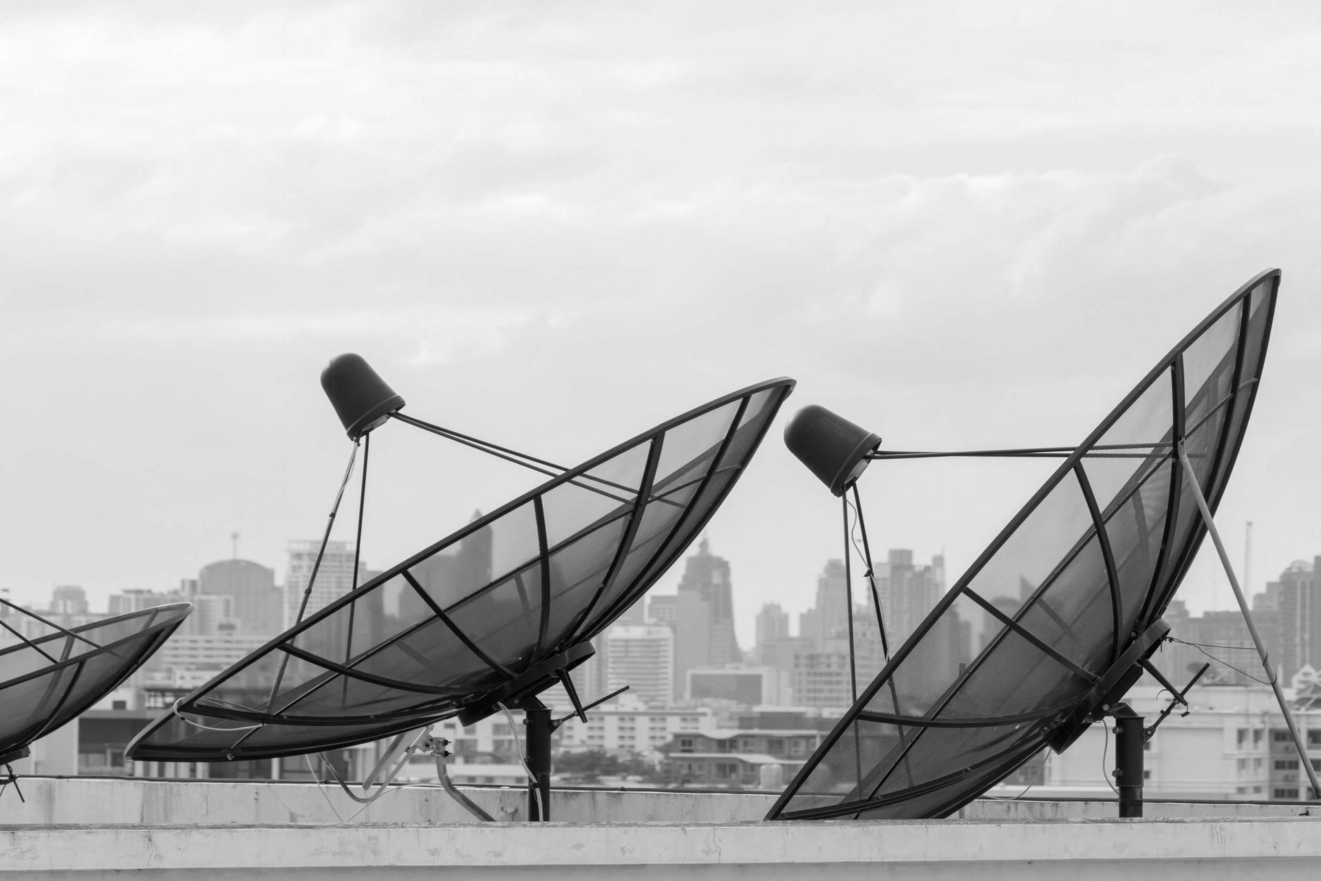 Una fotografía en blanco y negro de tres antenas parabólicas en la parte superior de un edificio.